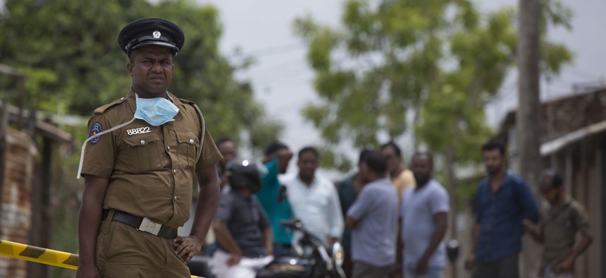 A police officer stand guards at a site of a gun battle between troops and suspected Islamist militants as neighbors gather to watch in Kalmunai, Sri Lanka, Sunday, April 28, 2019.