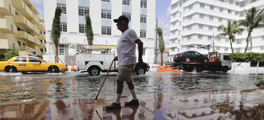 In this 2015 photo, Louis Fernandez walks along a flooded street in Miami Beach, Fla.