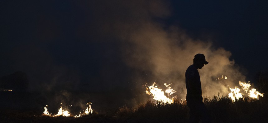 Neri dos Santos Silva, center, is silhouetted against an encroaching fire threat after he spent hours digging trenches to keep flames from spreading in the state of Mato Grosso, Brazil, Friday, Aug. 23, 2019.