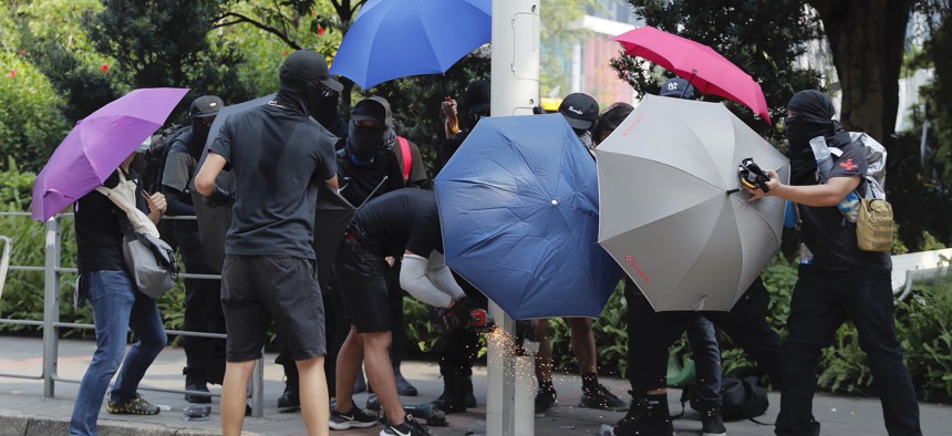 Demonstrators use umbrellas to shield themselves from view while they try to cut down a smart lamppost during a protest in Hong Kong, Saturday, Aug. 24, 2019. 