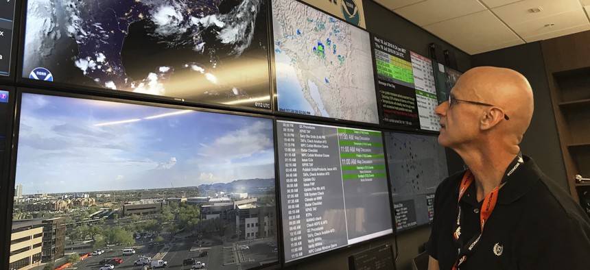 n this Wednesday, July 18, 2018 photo, National Weather Service forecaster Marvin Percha reviews monitors that track satellite and Doppler radar images, as well as his colleagues' forecasts posted on social media, at Tempe, AZ.