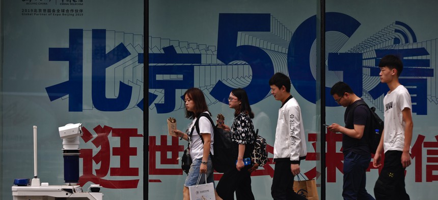 People walk toward a police robot mounted with surveillance cameras patrol past a 5G network advertisement at a shopping district in Beijing, Wednesday, May 15, 2019. 