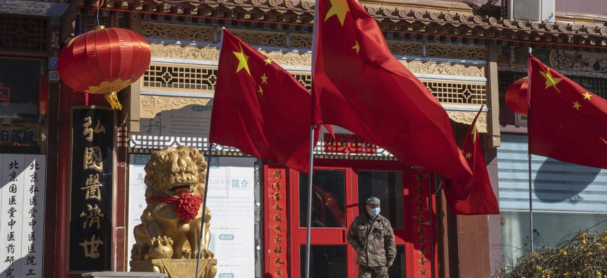 In this photo taken Tuesday, March 3, 2020, a worker stands near Chinese national flag and propaganda which reads "Go China" in Beijing. 