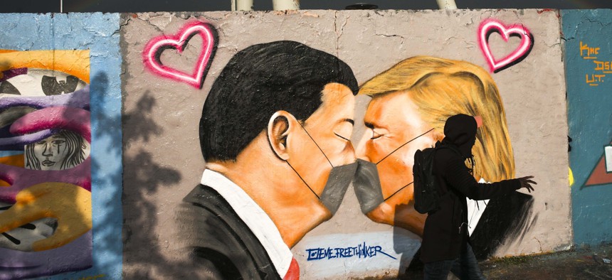 A man walks in front of graffiti depicting US President Trump, right, and China's President Xi Jinping kissing each other with face masks, displayed at a wall in the public park Mauerpark in Berlin, Germany, Wednesday, April 29, 2020. 