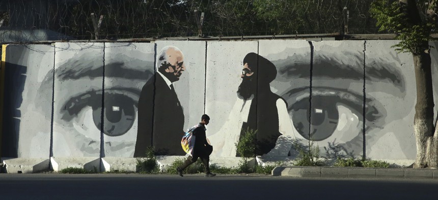 A young boy carries a sack of goods on his back walks past a wall depicting Washington's peace envoy Zalmay Khalilzad, left, and Mullah Abdul Ghani Baradar, the leader of the Taliban delegation, in Kabul, Afghanistan, Tuesday, May 5, 2020.