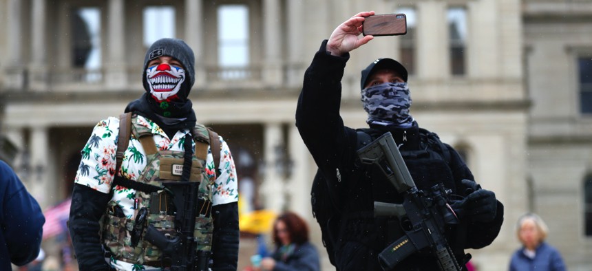 In this April 15, 2020, photo, protesters with rifles watch outside the State Capitol in Lansing, Mich.