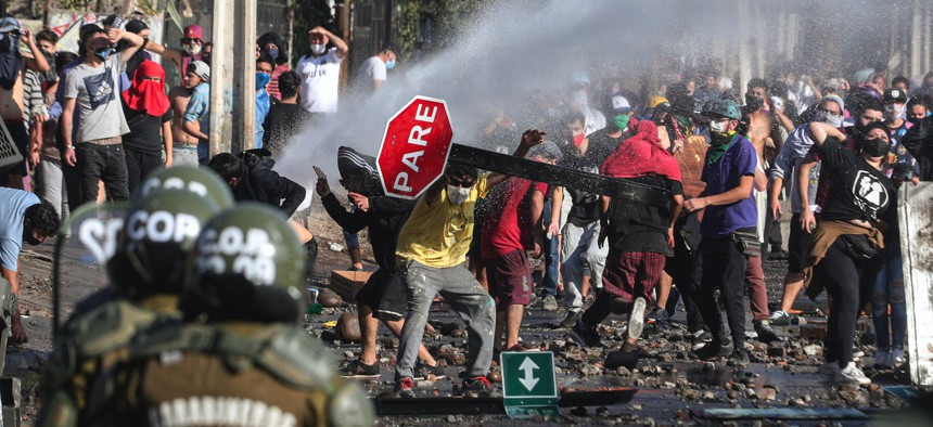 Demonstrators, some wearing protective face masks amid the new coronavirus pandemic, clash with the police during a protest demanding food aid from the government, at a poor neighborhood in Santiago, Chile, Monday, May 18, 2020.