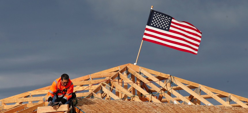 In this March 31, 2020, file photo the American flag flutters in the wind as work is done on the roof of a building under construction in Sacramento, Calif.