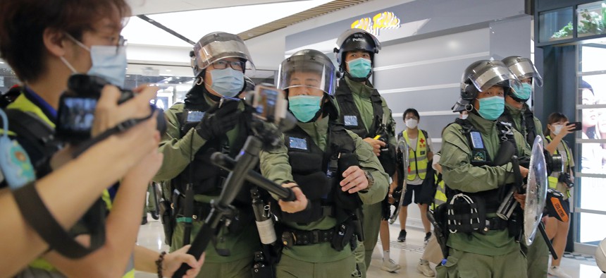 A riot police officer uses baton to hit a journalist's microphone during a protest to mark one-year anniversary of the Yuen Long subway attack, at a shopping mall in Hong Kong, Tuesday, July 21, 2020.