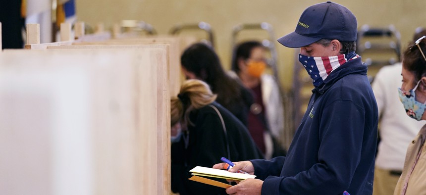 Bruce Lowell looks down at his ballot as he enters a voting booth at an early voting location, Tuesday, Oct. 27, 2020, in Lowell, Mass.