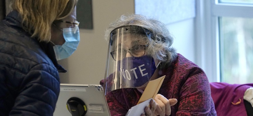 In this Oct. 28, 2020, file photo, poll worker Alice Machinist, of Newton, Mass., right, wears a mask and shield out of concern for the coronavirus while assisting a voter.