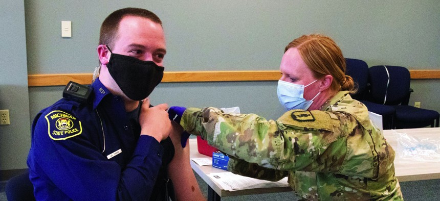 A Michigan Army National Guard medic gives a final dose of the COVID-19 vaccine to a Michigan State Police trooper at police headquarters in Dimondale, Michigan, March 4, 2021.