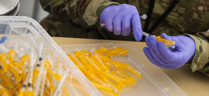 An airman assembles COVID-19 vaccine syringes.