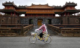 A woman covers her bicycle from the rain as she rides past the Hue Imperial Palace in central Vietnam's city of Hue on October 17, 2020.