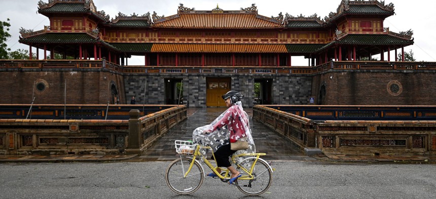 A woman covers her bicycle from the rain as she rides past the Hue Imperial Palace in central Vietnam's city of Hue on October 17, 2020.