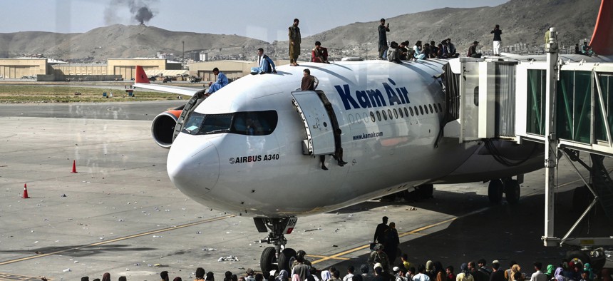 Afghan people climb atop a plane as they wait at the Kabul airport in Kabul on August 16, 2021.