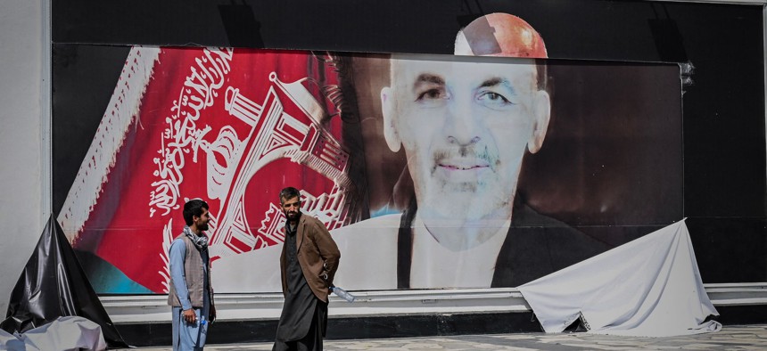 Afghan men stand next to a torn poster of Afghan President Ashraf Ghani at the Kabul airport in Afghanistan, August 16, 2021. 