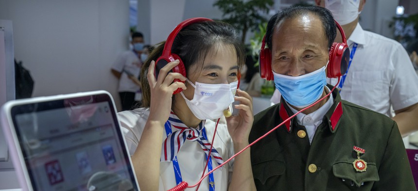 An attendant demonstrates a display for an elderly Chinese military veteran at a booth for Chinese telecom provider China Telecom at the PT Expo in Beijing, Sept. 28, 2021.