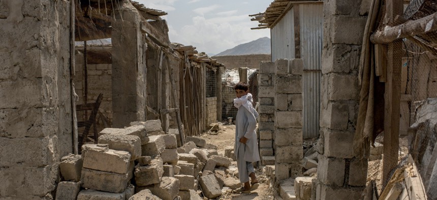 In this photo from July 2017, a boy walks through buildings damaged during fighting against the Islamic State of Iraq and Syria - Khorasan, or ISIS-K, in Nangarhar province, Afghanistan. 