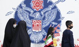 An Iranian schoolgirl carrying an Iran flag walks past an anti-U.S. mural on a wall of the former U.S. embassy after a ceremony to mark the anniversary of the seizure of the U.S. embassy in downtown Tehran, November 4, 2021. 