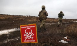 Ukrainian troops walk past a metal plate that reads as "Caution mines" on the frontline with Russia-backed separatists near Luganske village on January 11, 2022.
