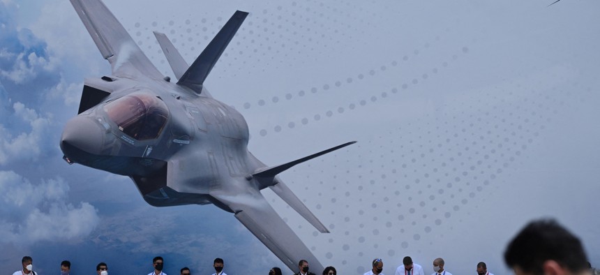 Visitors stand in the shade next to a display for Lockheed Martin as they watch the aerobatic display during the Singapore Airshow in Singapore on February 15, 2022.