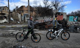 Men push their bikes past wrecked Russian military equipment in the city of Bucha, Ukraine.