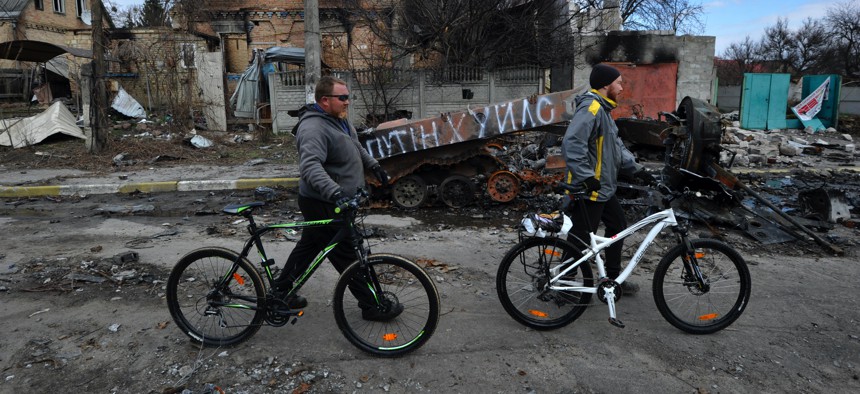 Men push their bikes past wrecked Russian military equipment in the city of Bucha, Ukraine.