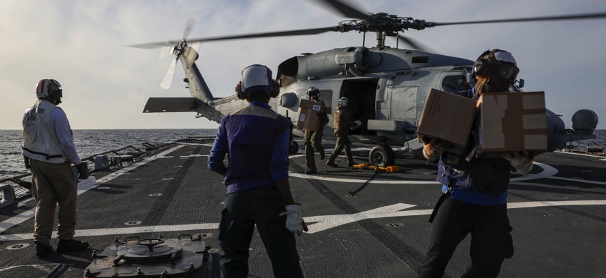 Sailors unload spare parts from an MH-60R Seahawk on the flight deck of the guided-missile destroyer USS Porter (DDG 78) on March 22, 2022.