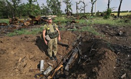 A Ukrainian serviceman stands in a shell crater next to destroyed Russian military vehicles on a field not far of the southern city of Mykolaiv on June 12, 2022, amid the Russian invasion of Ukraine. 