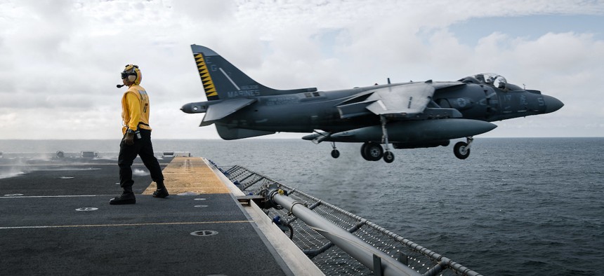 A U.S. Marine Corps AV-8B Harrier attached to the 22nd Marine Expeditionary Unit flies past U.S. Navy Aviation Boatswain's Mate (Handler) 1st Class Tu N. Chau during flight operations aboard the Wasp-class amphibious assault ship USS Kearsarge, Aug. 24, 2022.