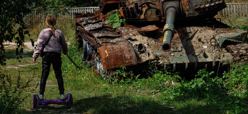 A teenager rides a hoverboard past a destroyed Russian army tank in the village of Lukashivka, Chernihiv region, on September 7, 2022, amid the Russian invasion of Ukraine.