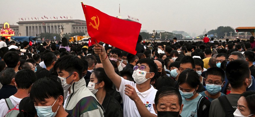 A man waves a flag of the Communist Party of China as people gather near Tiananmen Square during a flag-raising ceremony on China's National Day in Beijing on October 1, 2022.
