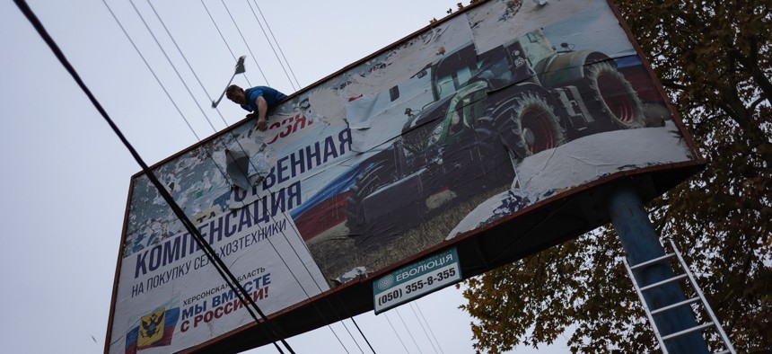 A local resident in recently liberated Kherson, Ukraine, tears apart a billboard emblazoned "We together with Russia" on November 13, 2022. 