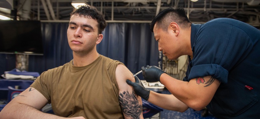Navy Petty Officer 2nd Class Mark Forrey administers a COVID-19 vaccine to Navy Seaman Micah Dayoub aboard the USS Ronald Reagan, in Yokosuka, Japan, Sept. 9, 2022. 