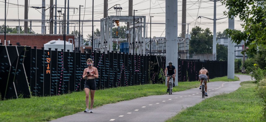 People pass a water treatment plant and electrical power lines on a a bike path in Arlington, Virginia on August 13, 2021. 