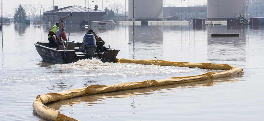 Contractors deploy a spill containment boom around the Offutt Air Force Base fuel storage area after flooding on March 18, 2019.