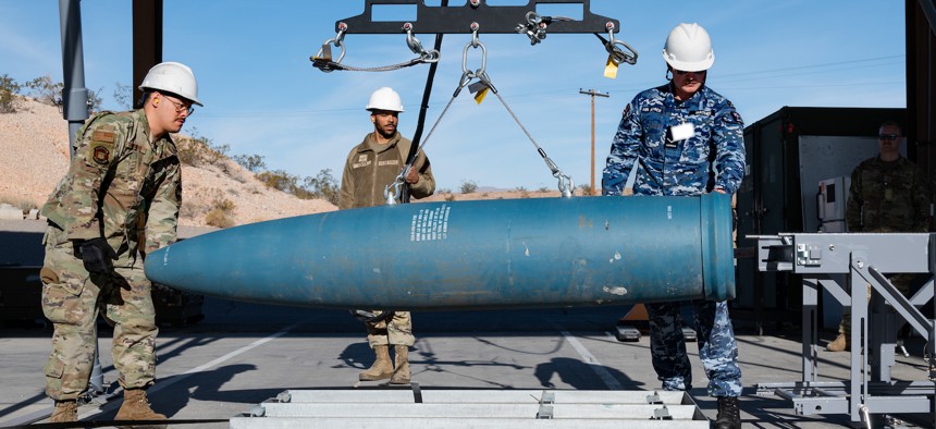 U.S. Air Force Senior Airman Tadeo Rodriguez, left, U.S. Air Force Staff Sgt. Jordan Render, middle, and Royal Australian Air Force Leading Aircraftman Luke Mather, right, upload an inert training bomb on the munitions assembly conveyor to load onto an F-35 during Red Flag, at Nellis AFB, Nevada, Jan. 18, 2024. 