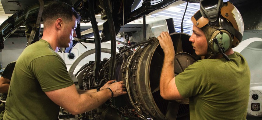 U.S. Marine Corps maintainers adjust cables on an engine of an MV-22 Osprey in the hanger bay of the USS Makin Island in 2016.