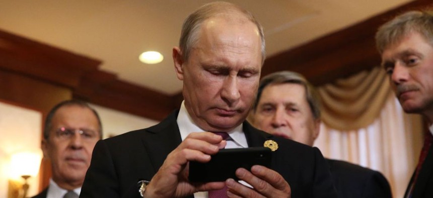 Russian President Vladimir Putin (C) holds an iPhone as his spokesman Dmitry Peskov (R) looks on prior to a meeting. 