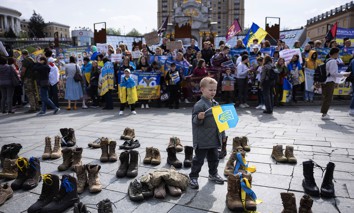 A boy holds a Ukrainian flag amid military boots arranged by the relatives and friends of missing Ukrainian soldiers during a demonstration in Kyiv, Ukraine, on April 13, 2024.