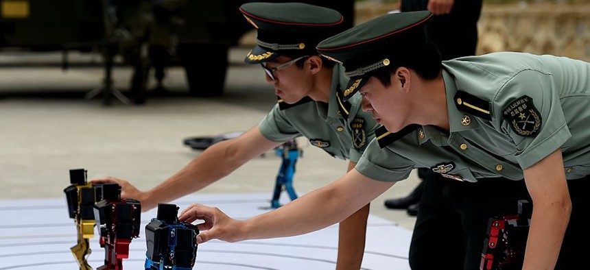 Chinese People's Liberation Army cadets adjust dancing humanoid robots at the PLA's Armoured Forces Engineering Academy in Beijing on July 22, 2014. China's military opened up its engineering academy to journalists on July 22, with demonstrations of rolling tanks, bayonet drills and dancing robots