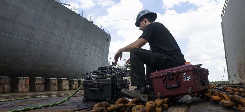 A shipyard worker and a "Toka" maintenance drone from Gecko Robotics.