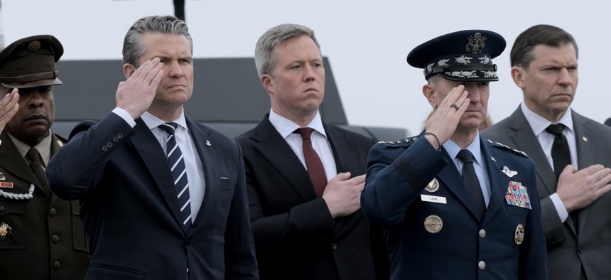 Defense Secretary Pete Hegseth, Army Secretary Dan Driscoll, and Joint Chiefs Chairman Gen. Dan Caine stand at attention as U.S. troops killed in the Iran war are brought home through Dover Air Force Base on March 7, 2026.