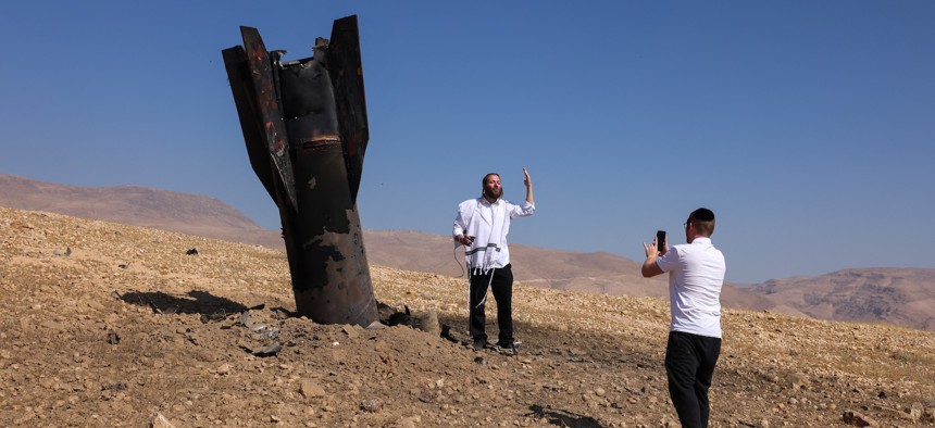 A man poses for a photo next to a fallen rocket half-buried in the ground on the outskirts of Jericho on June 8, 2026, following Iranian and Iran-backed Houthi rebel attacks.