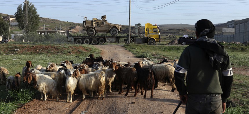 A Syrian shepherd watches as U.S. military equipment is hauled away from a base in Syria on April 16, 2026.