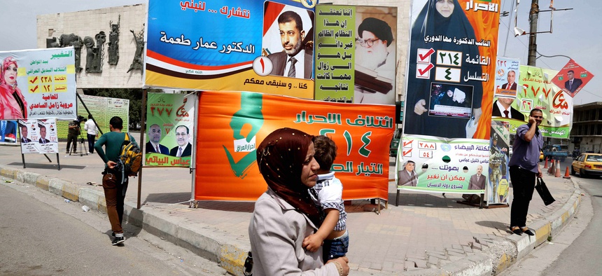 An Iraqi woman walks past a series of billboards advertising election candidates in Iraq