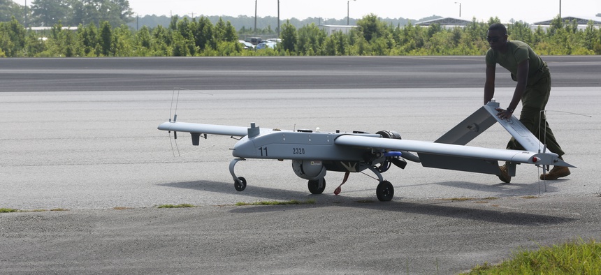 An avionics maintenance technician pushes an RQ7-B drone back to the taxiway after landing