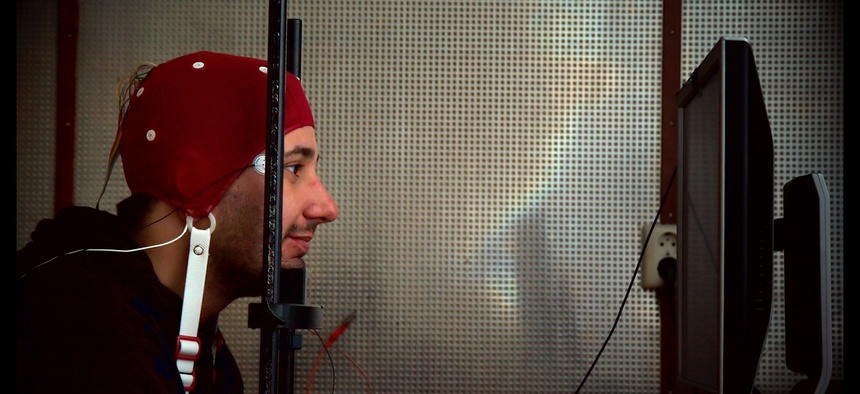 A man wears an EEG cap and stares into a computer screen as part of an experiment with brain-computer interfacing.