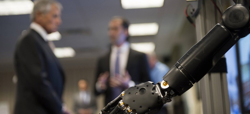 In the foreground, Defense Secretary Chuck Hagel learns about one of the prosthetics developed as part of DARPA's Revolutionizing Prosthetics program.